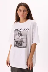 Remera color beige de corte amplio con mangas cortas y cuello redondo. Estampado frontal con la palabra "Monaco" en la parte superior y una fotografía en blanco y negro con la frase "Mont Carlo" en la parte inferior.