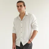 Camisa de algodón a rayas verticales celestes y grises claros, con cuello italiano y botones marrones.