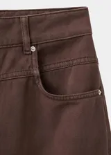 Pantalón de jean estilo wide leg color marrón chocolate, con tiro medio, cinco bolsillos, cierre frontal con cremallera y botón, y detalle de costuras en la cadera.