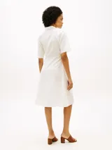 Vestido midi color blanco de Tommy Hilfiger, confeccionado en lino y algodón. Presenta cuello camisero, manga corta, cierre frontal oculto y un cinturón ajustable anudado en la cintura. La falda tiene diseño acampanado y largo por debajo de la rodilla.
