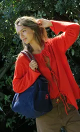 Bolso amplio de gamuza azul con manijas largas de cuero marrón. Cuenta con bolsillos laterales, uno con clip, cierre posterior y un bolsillo interno amplio. Presenta detalle de bandera y logo bordado en los laterales.