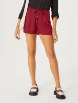 Short de vestir color bordó, de tiro alto con cintura elástica fruncida y lazo ajustable. Presenta pliegues frontales y botones decorativos a los costados de la cintura.