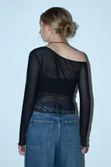 Remera de manga larga y escote asimétrico, confeccionada en tul negro transparente. Lleva un top negro opaco debajo y un cinturón de cadena plateada a la altura de la cadera.