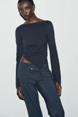 Camiseta de cuello barco y manga larga con diseño asimétrico en el bajo. Presenta un corte entallado con cierre lateral mediante cremallera oculta.