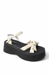 Sandalia de plataforma negra con tiras color crema y un moño decorativo en la parte delantera. Cierre de hebilla en el tobillo.