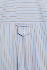 Camisa oversize de manga larga con cuello solapa, cierre frontal de botones y bolsillo de parche en el pecho, con diseño de rayas verticales celestes y blancas.