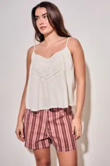 Blusa color off white de algodón peinado, sin mangas, con tirantes finos, escote en V con detalles de encaje y bordados, y pliegues decorativos en los laterales.