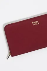 Billetera grande de nylon color negro con cierre perimetral de cremallera. Presenta un tirador de cordón bicolor con terminales metálicos y el logo de la marca estampado en dorado en el frente.