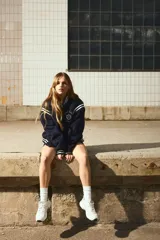 Campera de béisbol azul marino, ligeramente acolchada y confeccionada en tejido polar suave. Presenta cuello, puños y bajo acanalados con rayas blancas, hombros caídos, cierre frontal de botones a presión y bolsillos laterales ribeteados. Lleva un bordado en el pecho con texto que incluye "MILANO FIRENZE ITALIA".