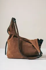 Cartera tipo hobo de gamuza color marrón, con correa trenzada de cuero negro y detalles laterales en cuero negro.