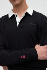 Remera polo de manga larga azul con cuello camisero blanco y cierre frontal de botones ocultos. Presenta un pequeño bordado con el texto "uniform" en el pecho y calce relajado.