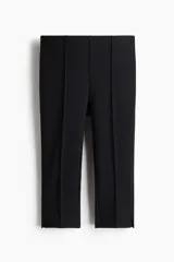 Leggings capri negros de punto grueso, con elástico oculto en la cintura, pliegues cosidos adelante y atrás, y pequeña abertura en los bajos.