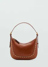 Bolso de hombro tipo hobo color marrón, confeccionado en efecto piel con detalle de tachuelas metálicas doradas en los bordes. Cuenta con asa ajustable con hebilla y cierre de cremallera superior.