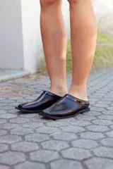 Zapatos tipo mules de cuero negro, con punta fina y detalle de charol en el borde superior.