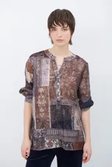 Camisa de corte recto con cuello mao y cierre frontal parcial de botones. Presenta un diseño estampado tipo patchwork con motivos florales y geométricos en tonos tierra, marrones y beige. Posee mangas tres cuartos con puños simples.