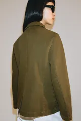 Chaqueta de estilo utilitario color verde militar, con cuello solapa, manga larga y cierre frontal con botones ocultos por solapa. Presenta bolsillos con solapa en la parte delantera y un bolsillo de plastrón en el pecho.