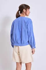 Cazadora azul de manga larga con puños elásticos, cuello redondo sin solapas y cierre frontal con botones grandes de color claro.