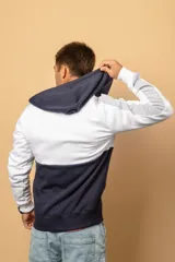 Campera con capucha y cierre frontal, con diseño en bloques de color blanco, azul marino y gris, mangas largas con puños elastizados y bolsillos tipo canguro.