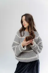 Buzo de tejido de punto grueso en color gris con rayas horizontales en color crema, de corte holgado, cuello redondo y mangas largas.