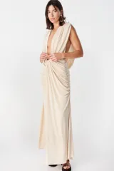 Vestido largo de fiesta color beige, con escote profundo en V, diseño drapeado en la cintura y espalda descubierta con caída fluida.