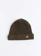 Gorro tipo beanie de punto inglés en color marrón oscuro, con diseño de doble capa y etiqueta de cuero sintético con logo en el frente.