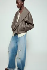 Cazadora Zara Woman Collection de efecto piel con cuello solapa ancho, manga larga, bolsillos delanteros y bajo elástico. Presenta un cierre frontal cruzado con botón a presión.