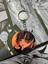 Llavero redondo con ilustración de personaje de anime con pelo negro y fondo naranja.