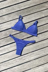 Conjunto de bikini color azul brillante con acabado metalizado. El top es de estilo triangular con breteles regulables y cierre de gancho en la espalda. La bombacha es de corte vedetina con laterales fruncidos elásticos.