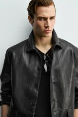 Sobrecamisa de corte relaxed fit confeccionada en tejido efecto piel de color negro, con cuello solapa, manga larga, bolsillos con solapa en la cadera y cierre frontal de botonadura.