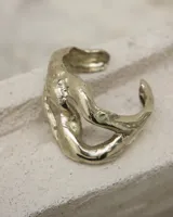 Brazalete abierto de diseño orgánico y voluminoso, con acabado metálico brillante. Su forma irregular y ergonómica permite un ajuste cómodo en la muñeca o antebrazo.