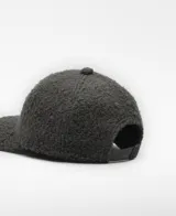 Gorra de seis paneles color gris oscuro, confeccionada en tejido de lana y poliéster con textura afelpada o borreguito. Presenta un logo bordado en el frente.