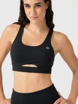 Top deportivo negro con escote redondo, tirantes anchos y un corte debajo del busto que crea una abertura. Incluye logo blanco en el pecho.