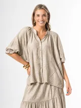 Camisa oversize color beige con estampado sutil, cuello mao, mangas raglán abuchonadas con puños elásticos y cierre frontal de botones.