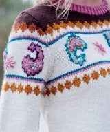 Vestido midi de punto color marfil, confeccionado artesanalmente en lana merino, con silueta en A, mangas largas oxford y cuello a la base. Presenta un diseño de bloques de color con bordados hechos a mano con motivos paisley y florales en tonos marrones, azules y rosados en la parte superior y las mangas.