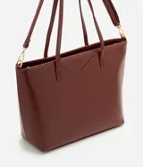 Cartera tipo shopper grande de Satinato, confeccionada en poliuretano con textura efecto crocco en color marrón. Presenta doble asa fija, correa larga desmontable con herrajes dorados y cierre superior por cremallera.
