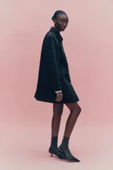 Abrigo de largo hasta la rodilla, confeccionado en mezcla de lana, color negro con textura sutil a cuadros. Presenta un corte evasé, cuello solapa, cierre frontal con botones dorados y bolsillos laterales insertados.