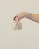 Charm en forma de mini bolso azul, con asas superiores y gancho tipo mosquetón, confeccionado en tela con etiqueta de la marca.
