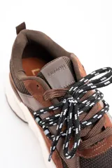 Zapatilla urbana de diseño chunky, combinando paneles de gamuza y cuero en tonos chocolate con malla técnica. Presenta cordones bicolores y una suela de plataforma de goma en color crema.