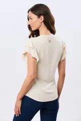 Camisa de lino y viscosa color beige, con cuello mao, escote en V y botones frontales de madera. Presenta mangas cortas con volados delicados.
