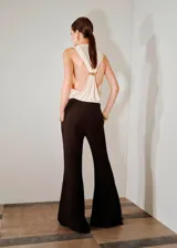 Pantalón flare de tiro medio, color marrón oscuro, con aberturas laterales en el bajo, bolsillos laterales y bolsillos de ribete en la parte posterior. Cierre oculto con botón, gancho y cremallera, e incluye forro interior.