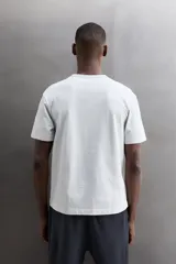 Camiseta de algodón gris melange con cuello redondo, mangas cortas y efecto lavado. Presenta un estampado de texto frontal en color oscuro con efecto desgastado.