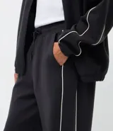 Pantalón deportivo de corte recto y estilo holgado, color negro con una línea vertical blanca en los laterales. Cuenta con cintura elástica con cordón de ajuste y bolsillos laterales.