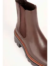 Bota tipo Chelsea de color negro, con elásticos laterales, suela track y taco cuadrado con detalle en tono marrón.