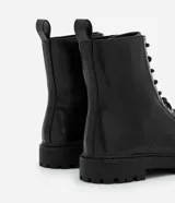 Bota estilo coturno de caña media, confeccionada en poliuretano con acabado liso. Presenta cierre mediante cordones frontales con ojalillos metálicos y suela track robusta.