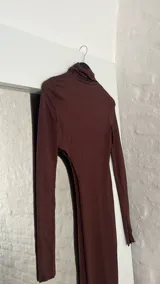 Top marrón de cuello alto y manga larga, con abertura en el abdomen y falda asimétrica.