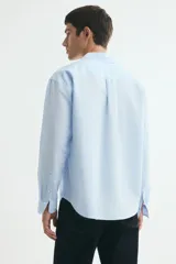 Camisa en mezcla de lino y algodón color celeste, de corte relajado, manga larga, con cuello inglés, bolsillo frontal y cierre de botones.