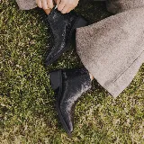 Bota corta de cuero vacuno con acabado metalizado y textura de reptil. Presenta punta fina, cierre lateral interno y taco cuadrado de madera.