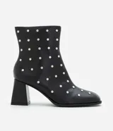 Bota de caña corta confeccionada en poliuretano color negro, con punta cuadrada, taco bloque y aplicación de studs metálicos en toda la superficie. Cuenta con cierre lateral.