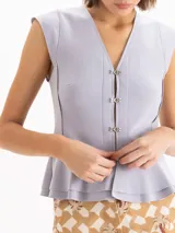 Top marrón ajustado al cuerpo, con escote en V y largo hasta la cadera. Cuenta con sisas estructuradas y cierre frontal con ganchos metálicos dorados. Presenta un doble volado en la parte inferior.