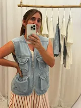 Chaleco de jean celeste con cierre frontal y múltiples bolsillos con botón.